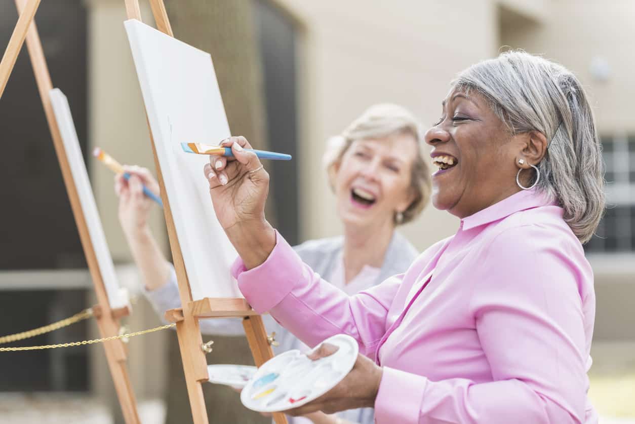 Two senior women having fun painting in art class